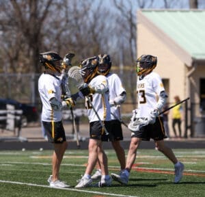 Lacrosse players celebrate a goal on the field, showcasing teamwork and athleticism during a sunny day.