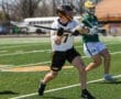 Lacrosse players compete on a sunny day, showcasing skills on the field during a match. Player in focus wears number 7.