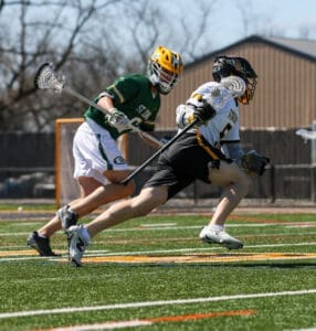 High school lacrosse players racing down the field during an intense match on a sunny day.