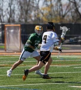 Two lacrosse players compete on a bright, sunny day, showcasing dynamic movement and athleticism on the field.