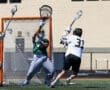 Goalie makes a crucial save during a high school lacrosse game in bright sunlight on a green field.