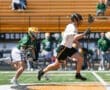 Lacrosse players in action: one sprinting with a stick while the other chases, showcasing competitive gameplay.
