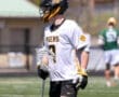 Lacrosse player in white jersey with Tigers logo, holding a stick on the field during a sunny day.