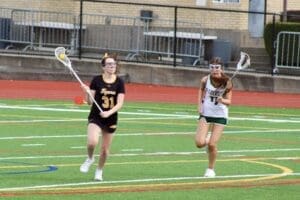 Two female lacrosse players compete on a vibrant field, showcasing athleticism and teamwork during a match.