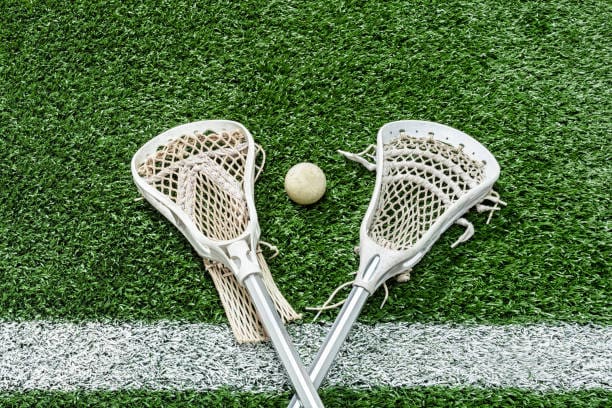 Two lacrosse sticks and a ball resting on green turf, ready for a game of lacrosse.
