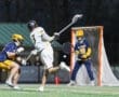 Lacrosse player in motion takes a shot on goal, with a goalie poised to defend during an evening match on a turf field.