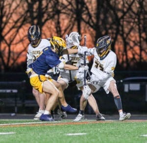 Two lacrosse teams competing fiercely during a game at twilight, showcasing teamwork and athleticism on the field.