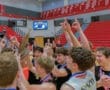 Celebrating team victory with a championship trophy in a gym filled with excited players and cheering fans.
