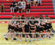High school boys' volleyball team huddling together on the court, showcasing teamwork and school spirit.