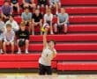 High school volleyball player preparing to serve a volleyball in front of an audience on red bleachers.