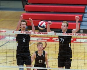 Two volleyball players block a shot at the net during a match at Peters Township High School's gym.