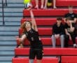 Volleyball player serves the ball with intensity, while spectators cheer from the red bleachers in the background.