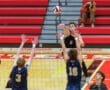 High school volleyball match with player #8 spiking the ball over the net as defenders jump to block.