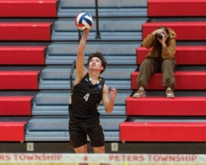 High school volleyball player #4 serves the ball during a match, with fans in the background capturing the moment.