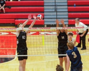 High school volleyball match at Peters Township, players block a spike at the net, showcasing competitive spirit and teamwork.