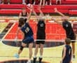 High school volleyball players compete at the net during a match, showcasing athleticism and teamwork in action.