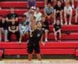 High school volleyball player #14 prepares to serve the ball, with an engaged crowd in the background.