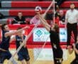 High school volleyball match action, featuring players jumping at the net. Spectators watch from the sidelines.