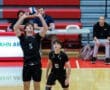 High school volleyball players in black uniforms preparing for a play in a gymnasium during a match.