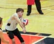 High school volleyball player receives a serve in an indoor gym, focusing intently on the ball during the game.