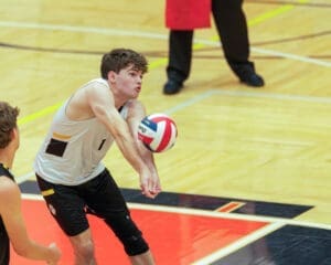 High school volleyball player receives a serve in an indoor gym, focusing intently on the ball during the game.