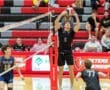 A male volleyball player sets the ball during a match, with spectators in the background, showcasing athletic competition.