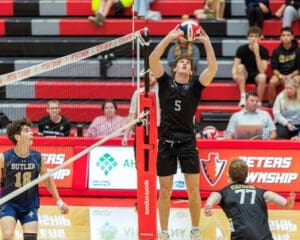 A male volleyball player sets the ball during a match, with spectators in the background, showcasing athletic competition.