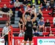 A young volleyball player in black jersey prepares to set the ball during a tournament match, with spectators in the background.
