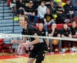 A focused volleyball player prepares for a play, with teammates and fans in the background during an exciting match.
