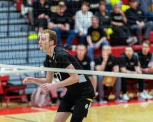 A focused volleyball player prepares for a play, with teammates and fans in the background during an exciting match.