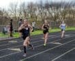 High school girls racing on a track field during a competitive athletic meet, showcasing determination and teamwork.