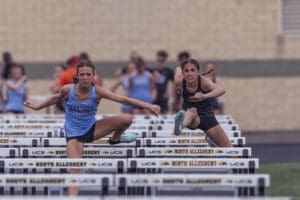 Two female athletes competing in a hurdle race, showcasing determination and athleticism on the track.