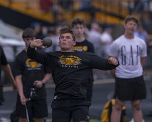 High school athlete competing in shot put during track and field event, showcasing focus and athleticism.