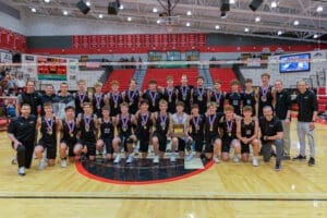 Boys volleyball team celebrating their championship win with medals and trophy on the court at Peters Township.