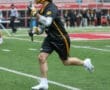 Lacrosse player in action on the field, wearing gear and running with a stick during a competitive game.