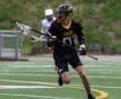 Player in a black lacrosse uniform running on a field with a stick, showcasing athleticism and team spirit.