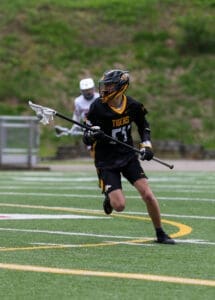 Player in a black lacrosse uniform running on a field with a stick, showcasing athleticism and team spirit.