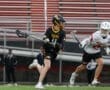 High school lacrosse match with players in black and white jerseys competing for the ball on a turf field.