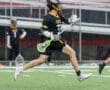 A lacrosse player in action, sprinting on a wet field while skillfully handling the stick and ball.