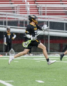 A lacrosse player in action, sprinting on a wet field while skillfully handling the stick and ball.