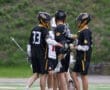 Boys' lacrosse team celebrates a play in the rain during a game on a green turf field.