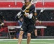 Lacrosse player in black uniform catching a ball during a rainy game, showcasing athleticism on the field.