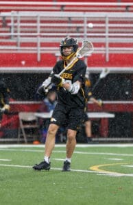 Lacrosse player in black uniform catching a ball during a rainy game, showcasing athleticism on the field.