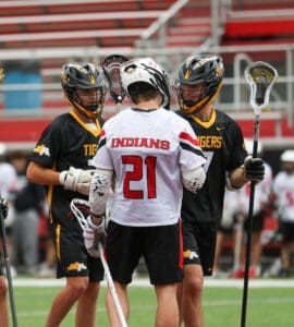 Lacrosse players in team jerseys discussing strategy during a game on the field, showcasing teamwork and athletic spirit.