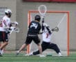 A lacrosse player in black attempts to score while the goalie in white makes a save during an intense game.