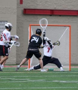 A lacrosse player in black attempts to score while the goalie in white makes a save during an intense game.