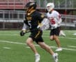 Player in black lacrosse uniform strides forward on field, showcasing teamwork and athleticism during a game.