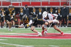 Two lacrosse players compete intensely for possession of the ball on a rainy field, showcasing athleticism and teamwork.