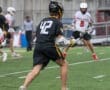 A young lacrosse player in a black jersey with the number 42 runs on a field during a rainy game.