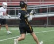 Lacrosse player in black jersey running on field during a rainy game, teammate in white jersey nearby.